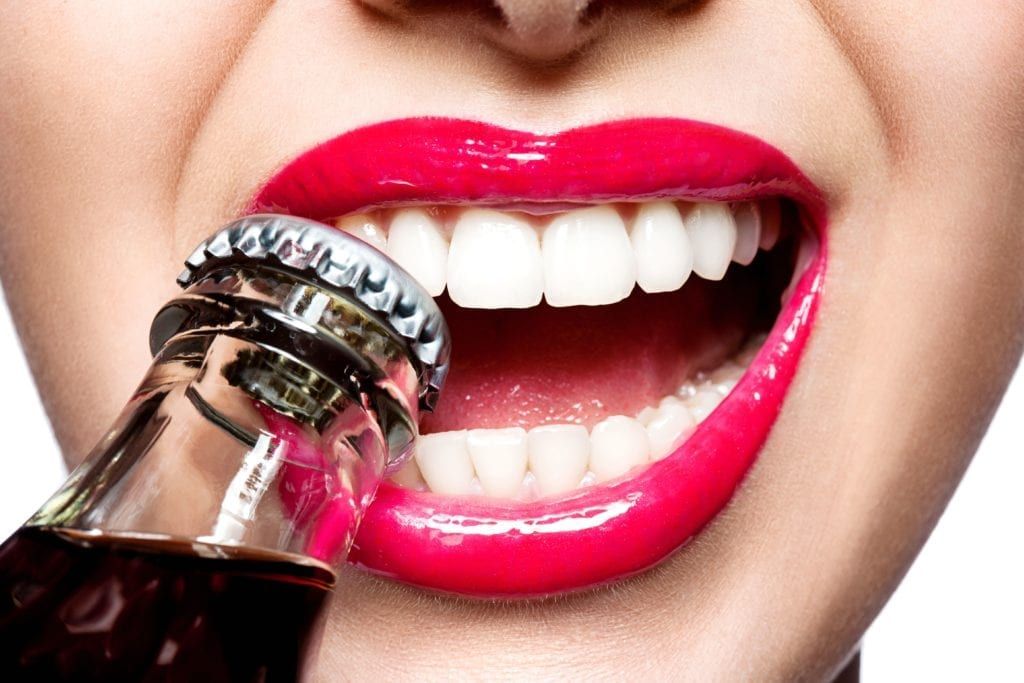 closeup of woman with lipstick using her teeth to remove bottle cap